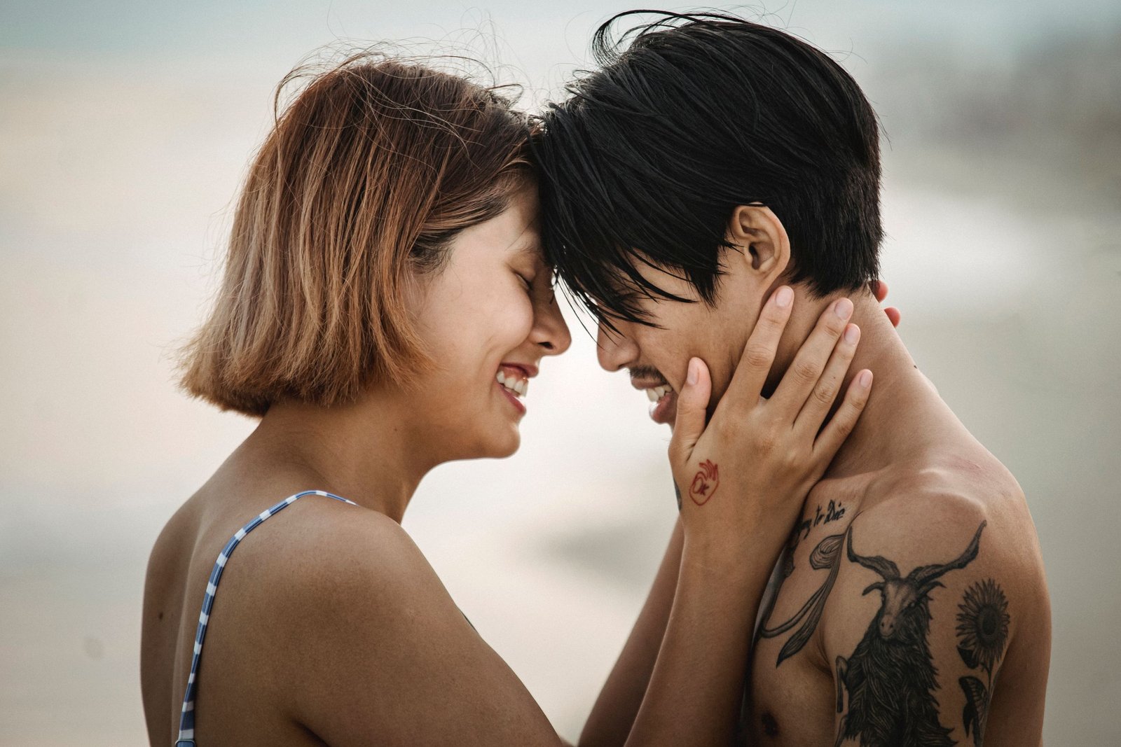 A loving couple with tattoos in an intimate embrace by the sea, sharing a moment of joy.