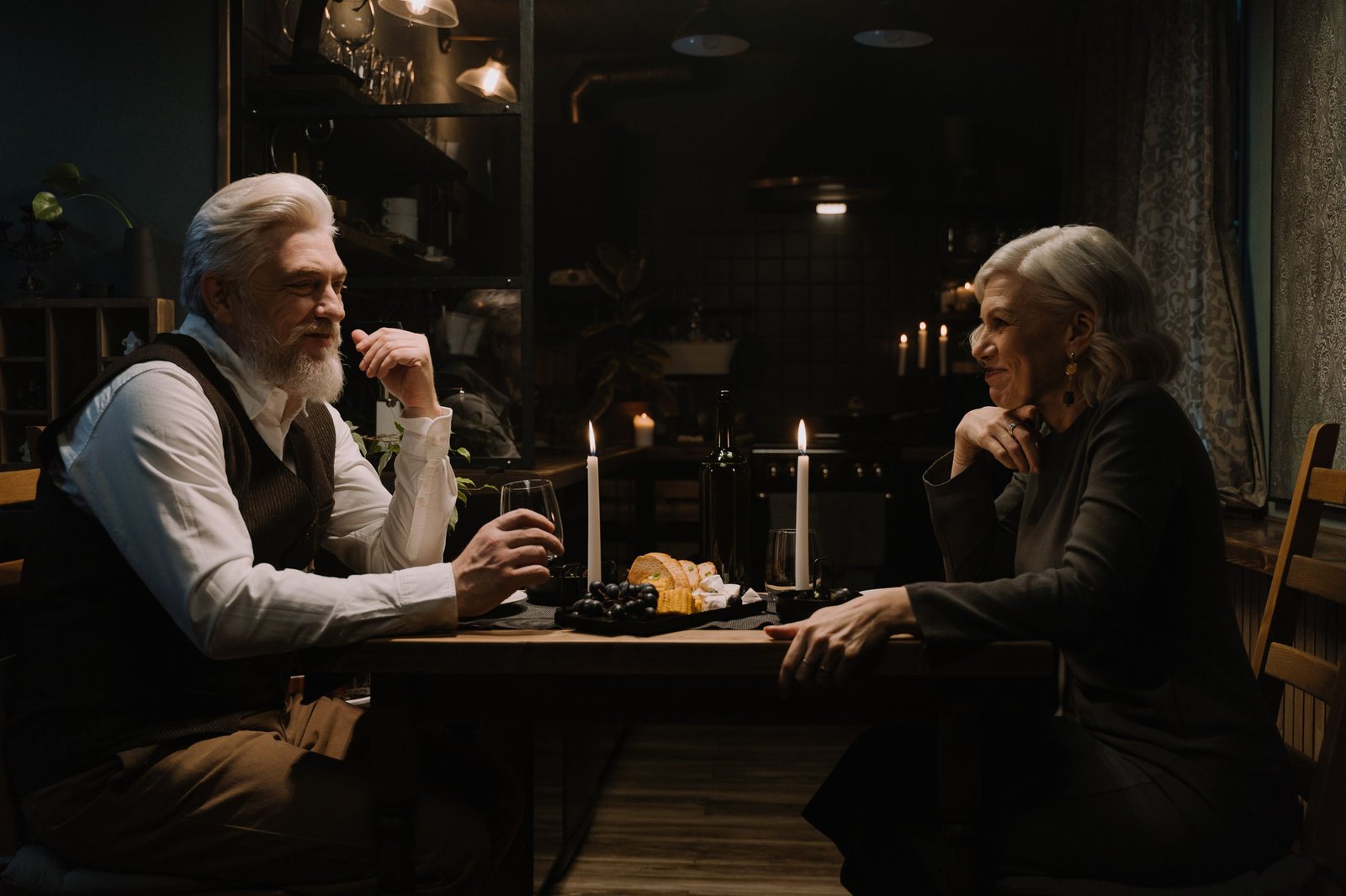 An elderly couple sharing a romantic dinner with candles and wine in a cozy room.