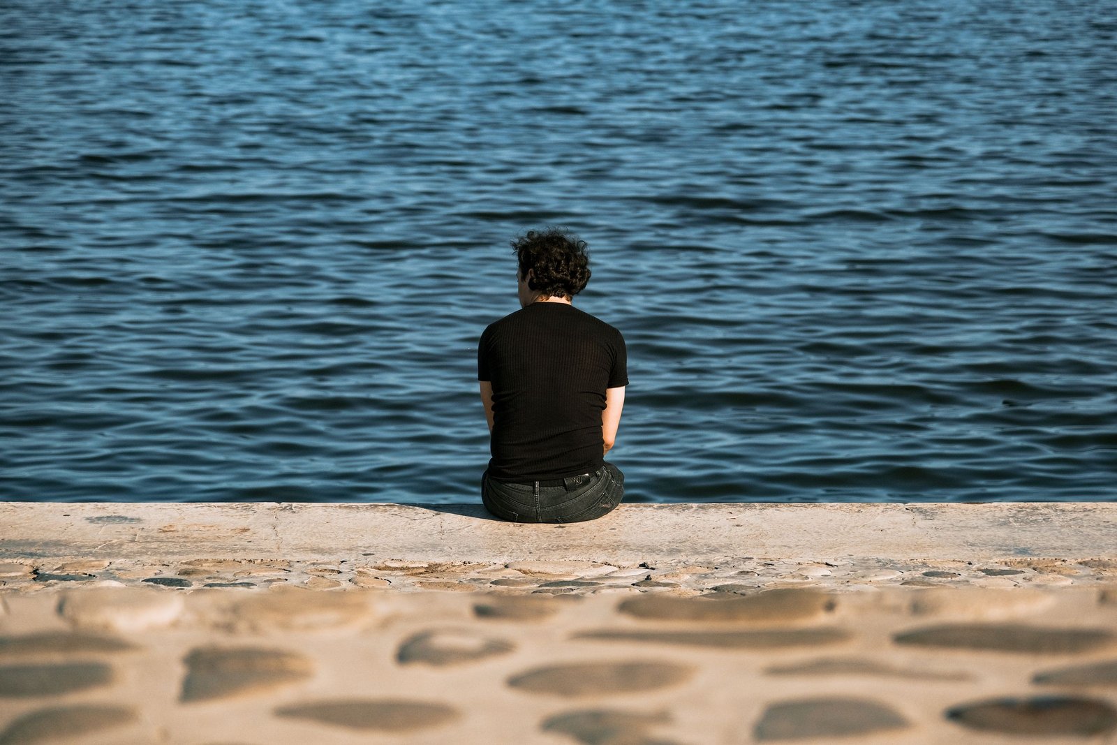 Contemplative view of a person sitting alone by the waterfront on a sunny day.