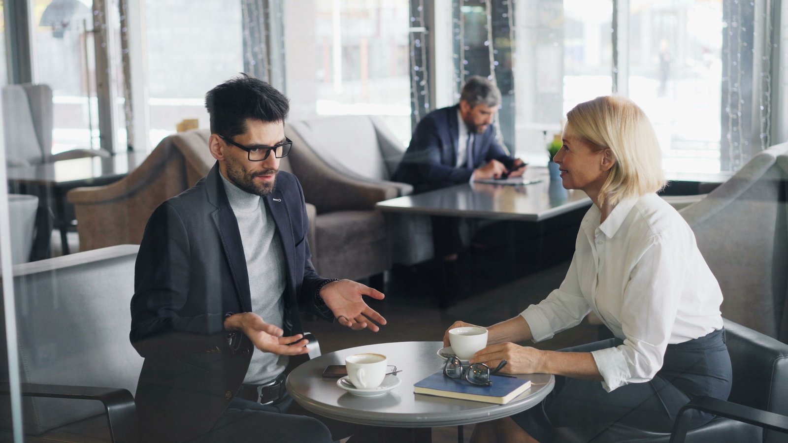 Professional colleagues discuss work over coffee in a contemporary café setting.