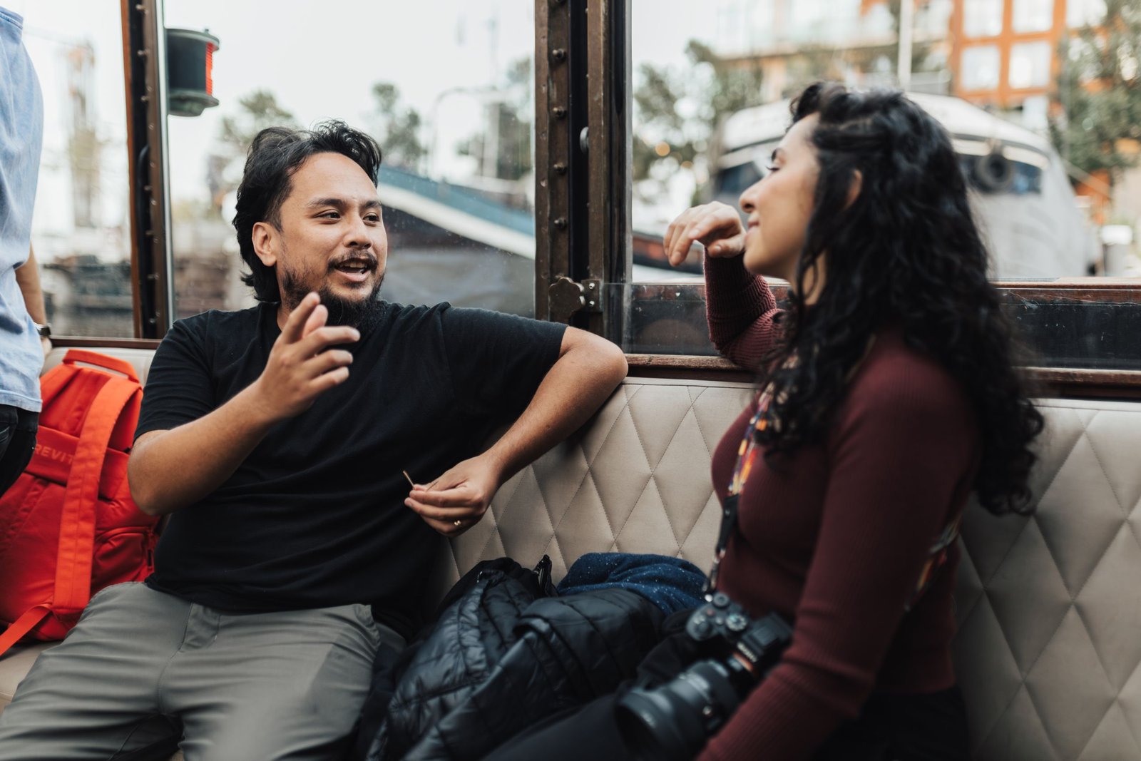 Two young adults engaging in a lively conversation while sitting indoors near a window.