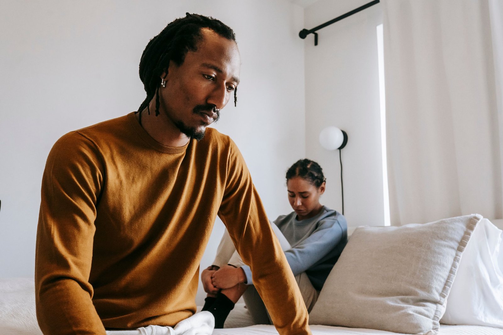 Young sad African American male near frustrated female partner sitting on bed during conflict at home